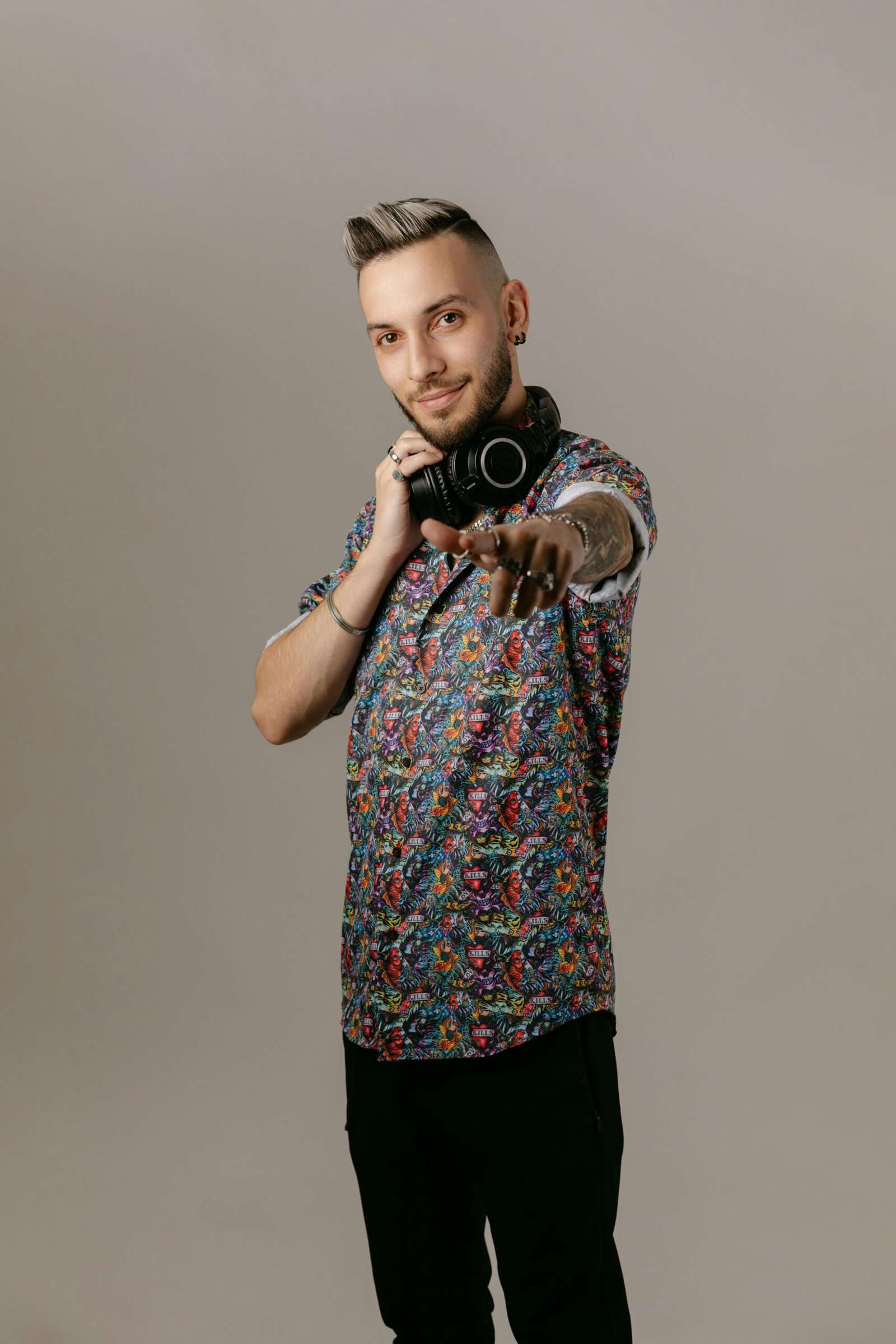 Stylish young DJ in floral shirt pointing with confidence and holding headphones