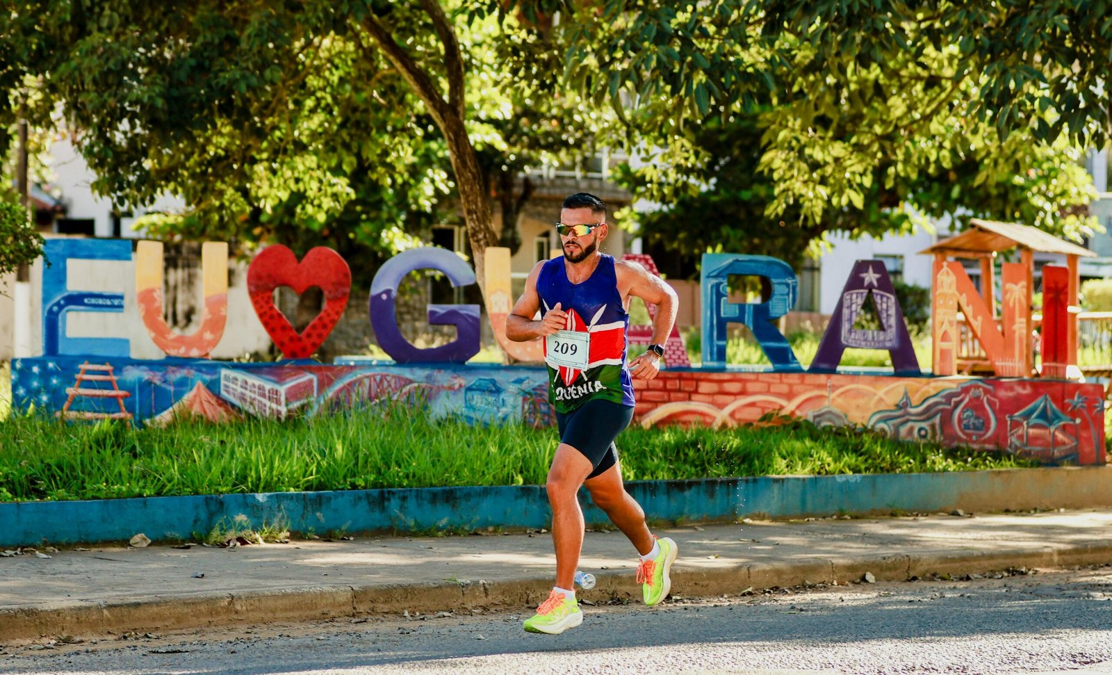 Athlete running in Guaraní with colorful street sign under lush trees.